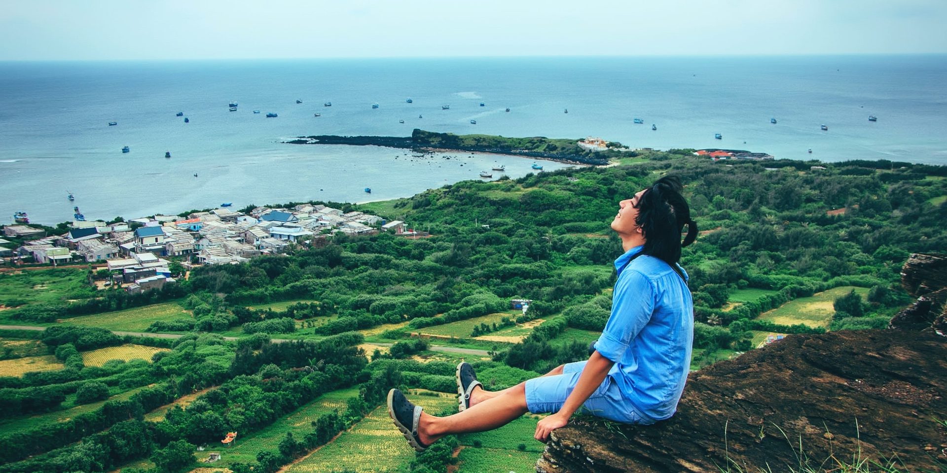 A person sitting on a cliff edge, looking out over the coast
